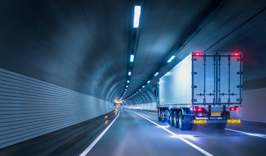 An articulated truck running through a lit road tunnel.